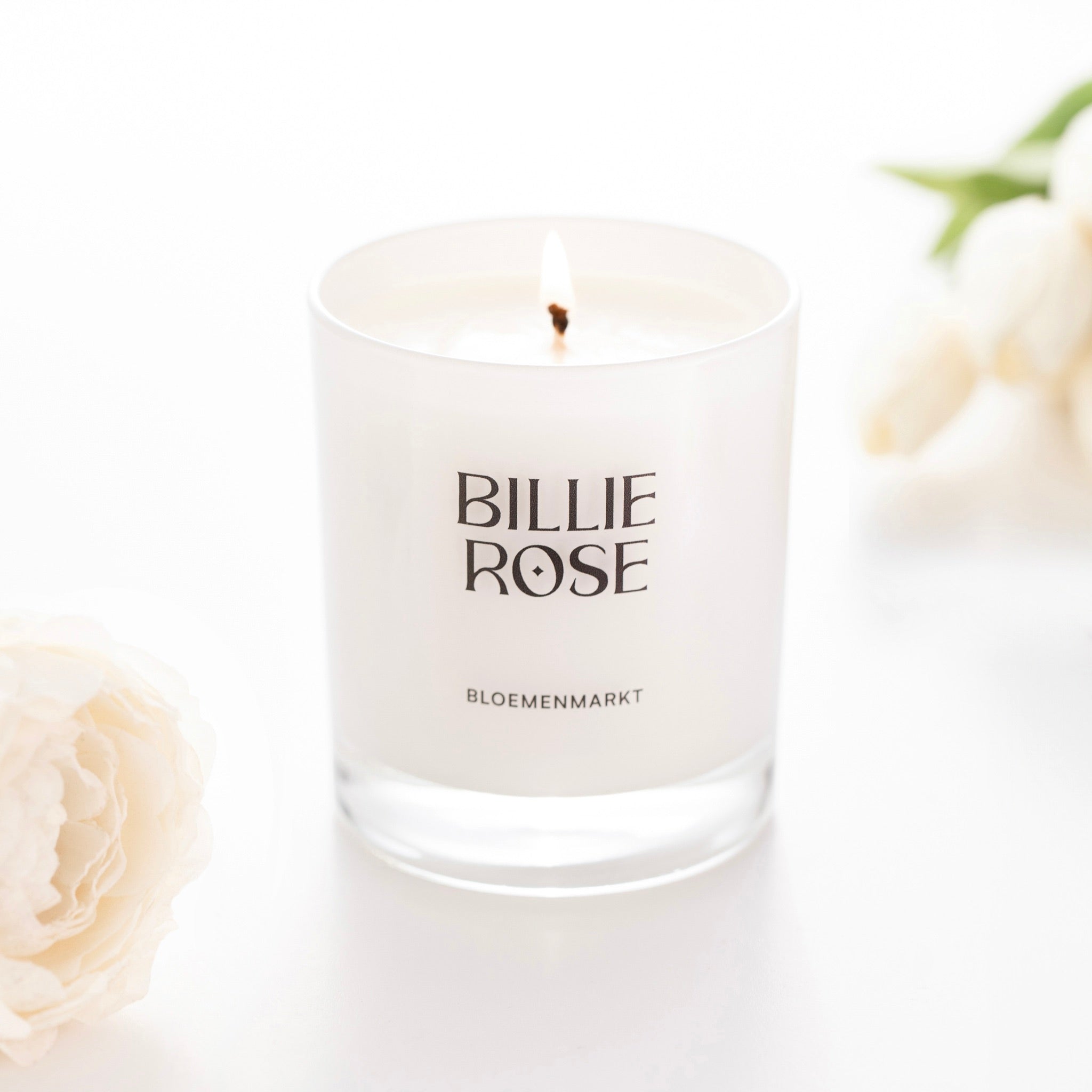 lit candle in white glass jar surrounded by two flowers