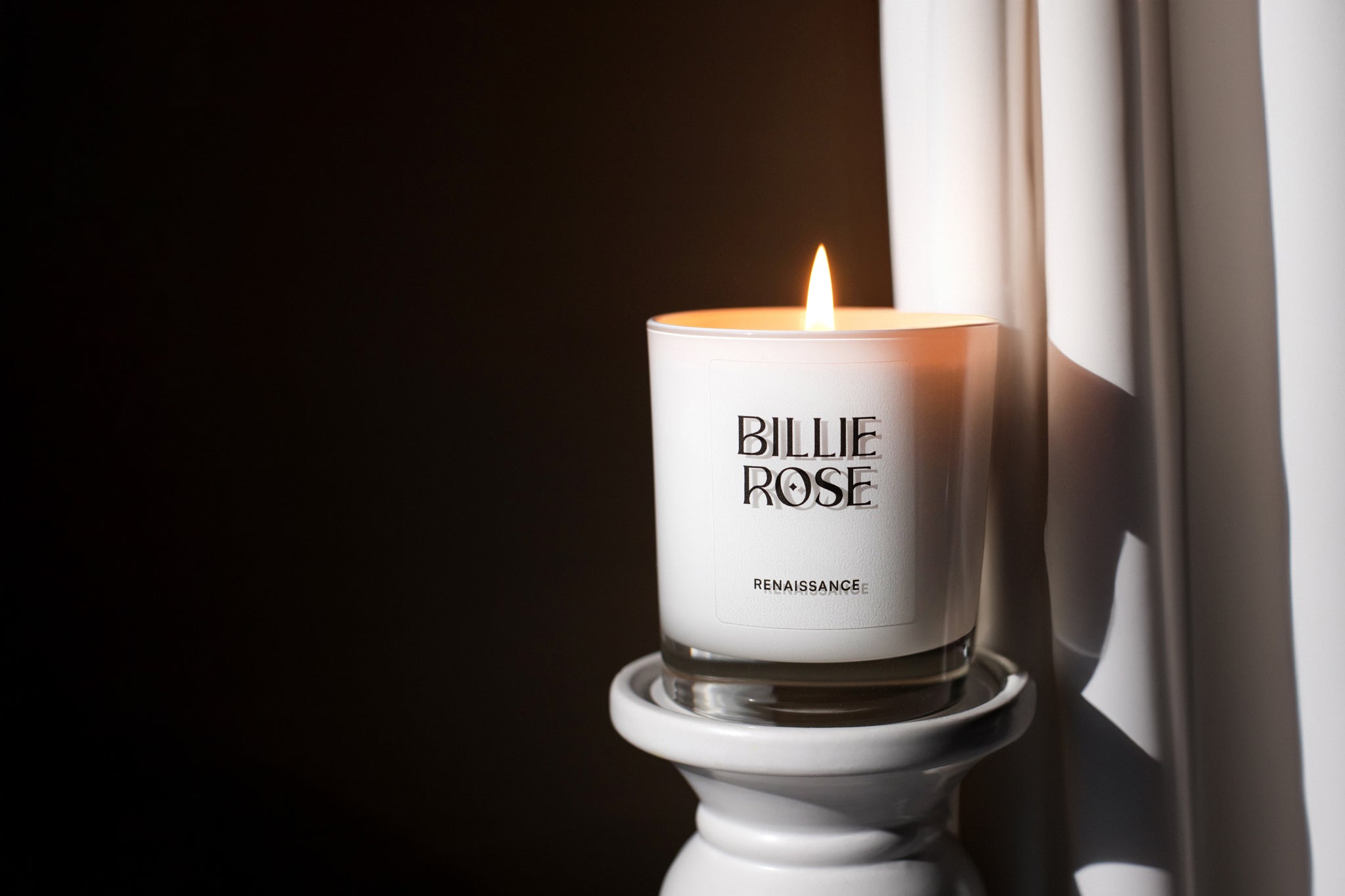 lit scented candle against a brown backdrop with curtain