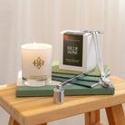 lit candle on books, box displayed behind it, candle wick trimmers and snuffer