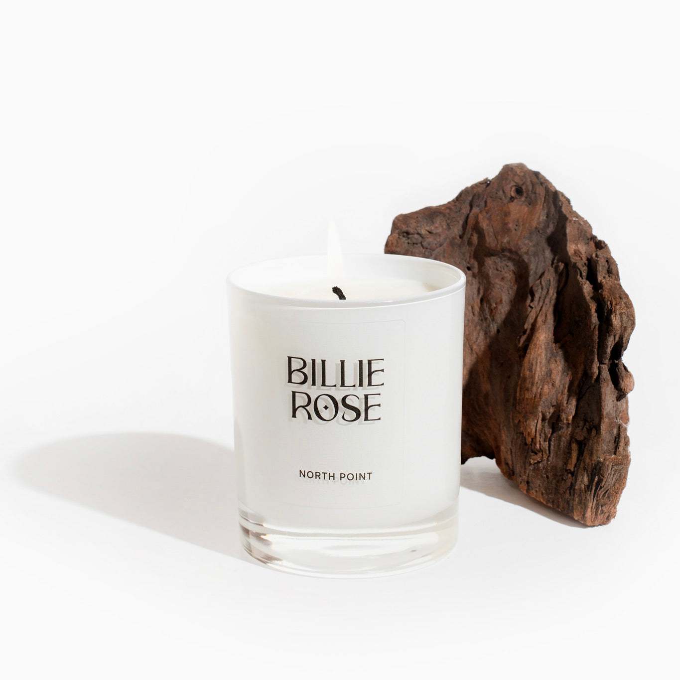 lit candle on white background with a piece of bark in the background